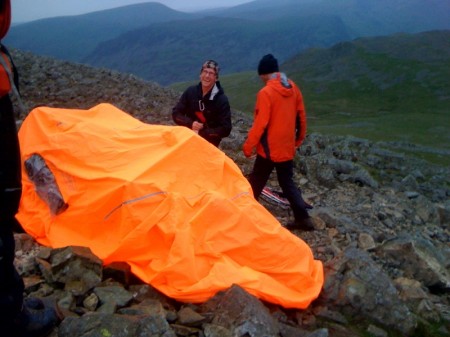 The casualty's leg is inspected by the team doctor under their very visible bivy tent